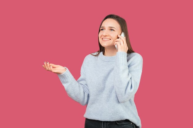 Foto de uma jovem sorridente falando ao telefone enquanto encolhe os ombros Studio atirou sobre fundo rosa