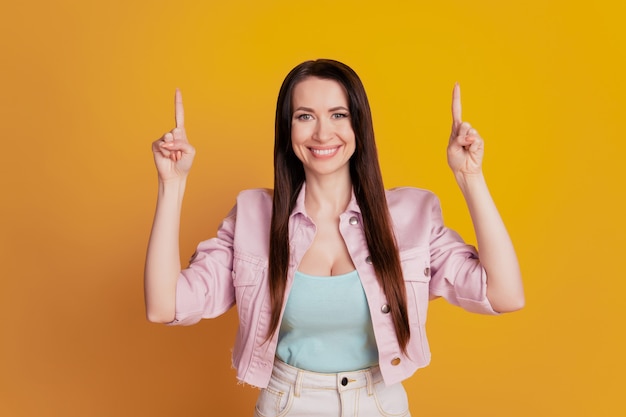 Foto foto de uma linda garota apontando para um espaço vazio isolado sobre um fundo amarelo