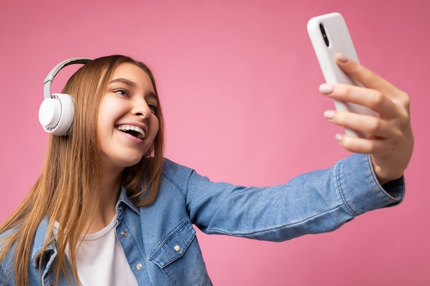 Foto de uma linda jovem loira sorridente feliz isolada sobre um fundo rosa vestindo branco