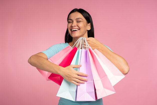 Foto de uma linda modelo milenar carregando muitos pacotes de compras e abraçando-a na frente da câmera com fundo rosa isolado