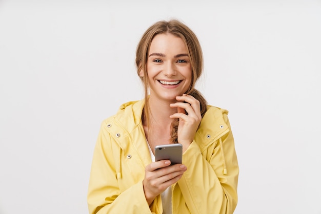 Foto de uma linda mulher alegre em uma capa de chuva usando o celular e sorrindo