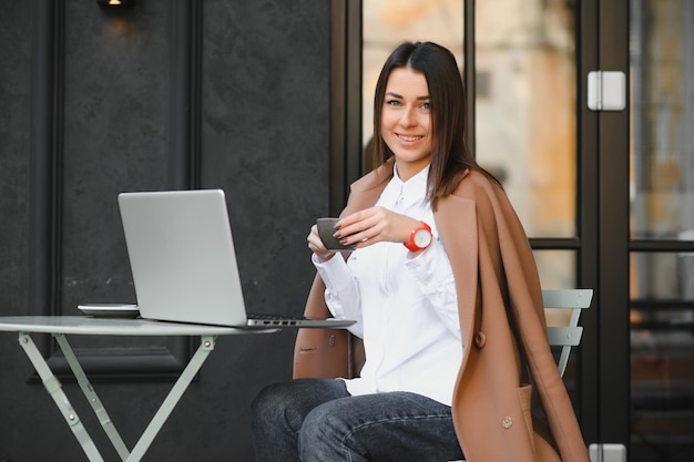 Foto de uma linda mulher atraente trabalhando em um laptop, digitando sentado no café, bebendo café