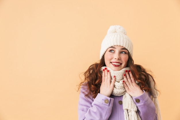 Foto de uma linda mulher de 20 anos com roupas de inverno, sorrindo, em pé, isolada