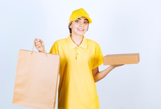 Foto de uma linda mulher de uniforme amarelo segurando uma caixa de papel artesanal em branco marrom e um saco.