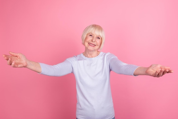 Foto de uma linda mulher envelhecida, de braços abertos, dá boas-vindas a um abraço amigável e hospitaleiro isolado sobre o fundo cor-de-rosa