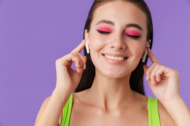 Foto de uma linda mulher feliz com maquiagem brilhante usando fones de ouvido e sorrindo