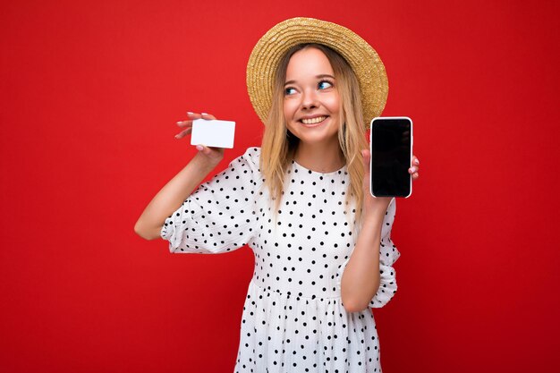 Foto de uma linda mulher loira sorridente e feliz com roupas de verão, mostrando o smartphone com a tela vazia