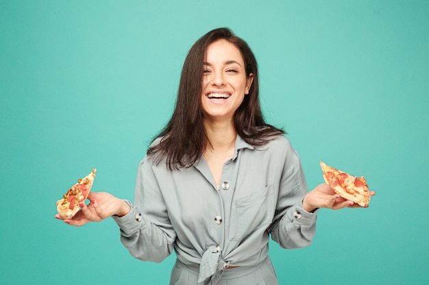 Foto foto de uma linda senhora segurando dois pedaços de pizza, saboreando junk food