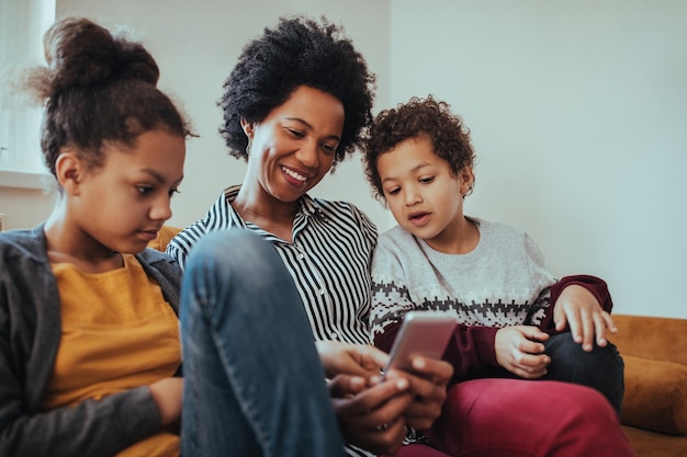 Foto de uma mãe e filhos usando um celular juntos em casa