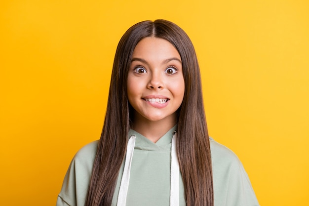 Foto de uma menina adorável criança engraçada vestida com roupa verde casual mordendo o lábio isolado fundo de cor amarela