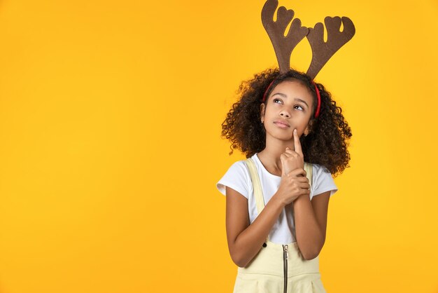 Foto de uma menina bonita com chifre na cabeça parecendo duvidosa isolada em fundo amarelo