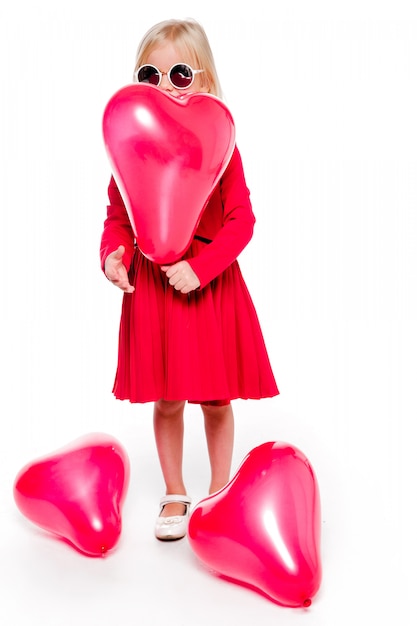 Foto de uma menina elegante em um vestido vermelho segurando um balão vermelho em forma de coração