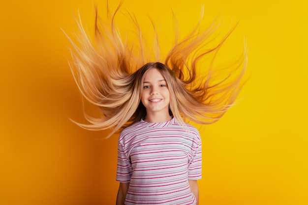 Foto de uma menina feliz com cabelo loiro voando isolada em um fundo amarelo