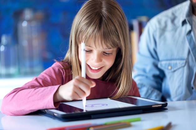Foto de uma menina muito feliz desenhando com tablet digital em casa.