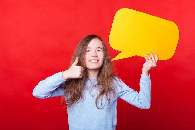 Foto de uma menina segurando um balão de fala vazio e mostrando o polegar