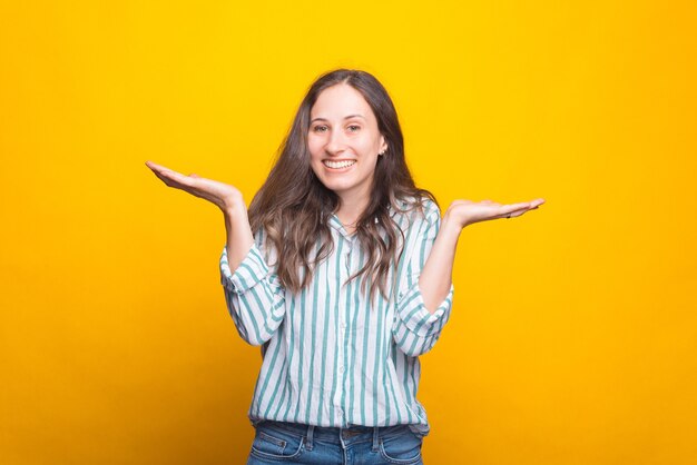 Foto de uma mulher alegre fazendo sinal de não sei perto de uma parede amarela