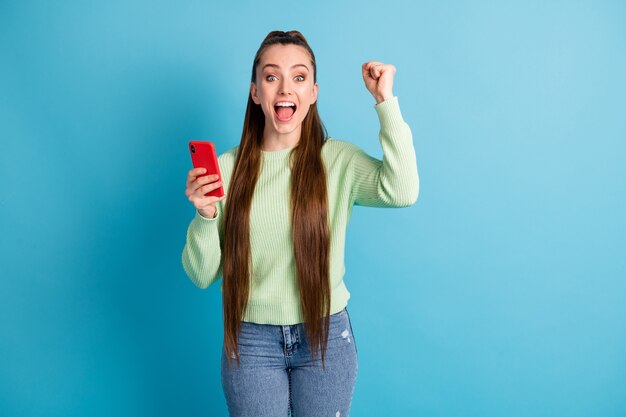 Foto de uma mulher alegre segurando o telefone com uma das mãos, o punho isolado em um fundo de cor azul pastel