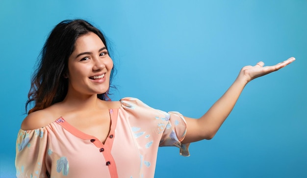 Foto de uma mulher asiática feliz vestida com roupas de verão sorrindo com um gesto de mão aberta em fundo azul