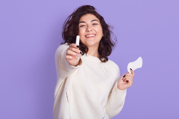 Foto de uma mulher caucasiana atraente segurando um tampão de algodão e um absorvente higiênico