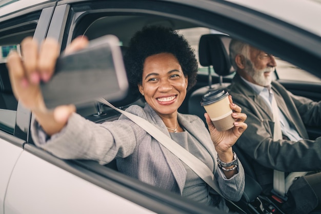 Foto de uma mulher de negócios negra sorridente tirando fotos com seu smartphone enquanto viaja de carro.