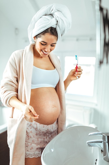 Foto de uma mulher grávida escovando os dentes no banheiro