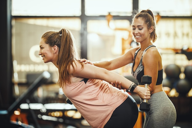 Foto de uma mulher grávida malhando com um haltere sob o controle do personal trainer feminino na academia.