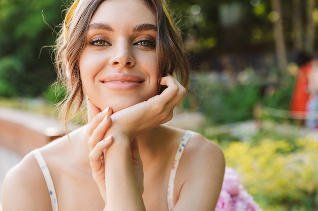 Foto de uma mulher jovem e bonita sorridente otimista em um parque verde