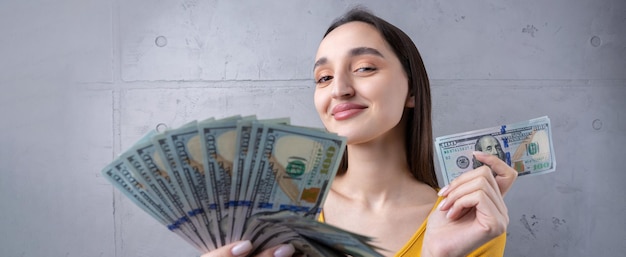 Foto de uma mulher rica em roupas simples segurando um leque de dinheiro em dólar isolado contra um fundo de parede de concreto