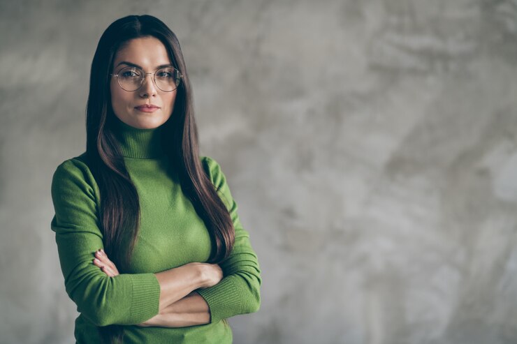 Foto de uma mulher séria, confiante e encantadora de cabelos compridos, com as mãos postas, olhando para você, com uma parede de concreto suspeito isolada.
