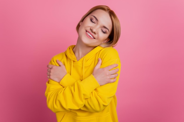 Foto de uma namorada adorável e fofa, abraçando os ombros e vestindo uma camiseta branca isolada em um fundo rosa