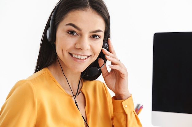 Foto foto de uma operadora de telefonia bem-sucedida usando fone de ouvido com microfone, sentada em seu local de trabalho no escritório e falando com o cliente