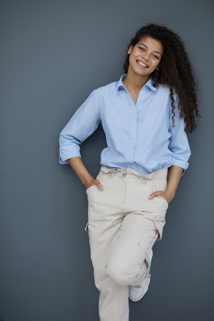 Foto de uma senhora alegre e autoconfiante, de braços cruzados, vestindo camisa azul, fundo de cor cinza