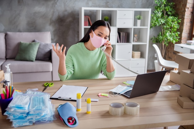 Foto de uma senhora asiática organizando pacotes de máscaras médicas para gripe facial para entrega de caixas conversando cliente falando de telefone fixo escreva a prancheta detalhes do pedido escritório em casa dentro de casa