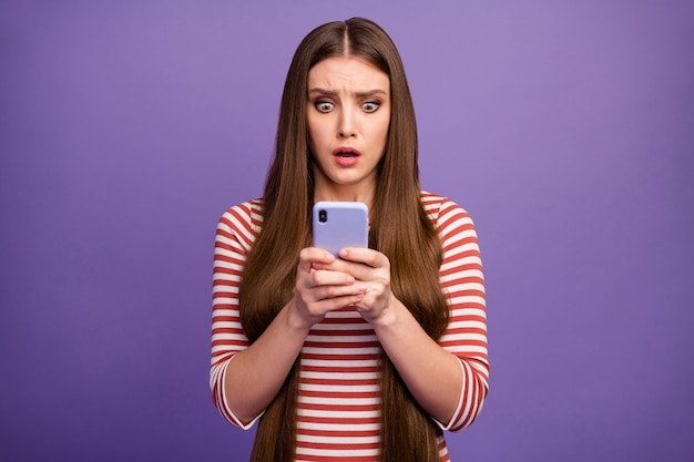 Foto de uma senhora atraente apavorada com olhar de boca aberta tela do telefone ler comentários negativos postagem do blog assustada vestir camisa listrada casual isolada parede cor roxa