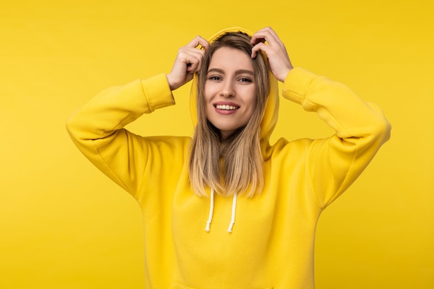 Foto de uma senhora atraente nas poses de capuz de uma forma bonita. Veste casuais com capuz amarelo, fundo de cor amarela isolado.