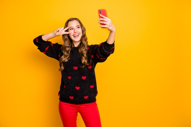 Foto de uma senhora bonita engraçada segurando as mãos do telefone tirando selfies enérgicos engraçados, mostrando o sinal V perto de óculos com padrão de corações.