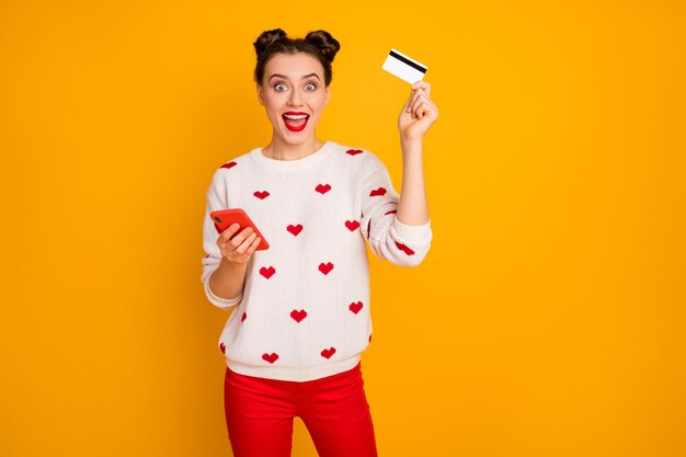 Foto de uma senhora bonita segurando telefone cartão de crédito de plástico fazendo compra on-line comprador viciado vestir padrão de corações pulôver branco