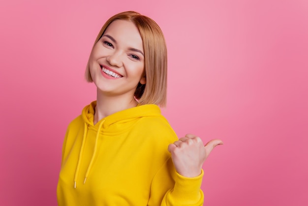 Foto de uma senhora loira alegre indica uma novidade de espaço em branco no polegar, use uma camiseta branca isolada em um fundo rosa