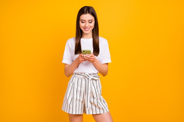 Foto de uma senhora muito atraente segurando as mãos do telefone lendo e-mail amigos convite para festa vestir camiseta branca casual listrada shorts de verão isolado parede de cor amarela vibrante