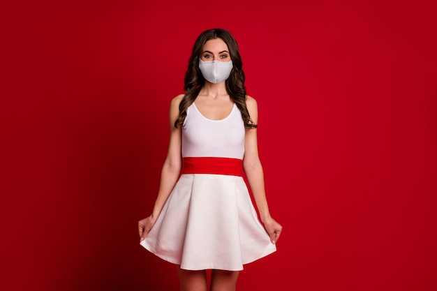 Foto de uma senhora muito fofa segurando uma saia ondulada de bom humor, uma pessoa sedutora, usando uma máscara de cobiça médica, vestido curto branco isolado fundo de cor vermelha