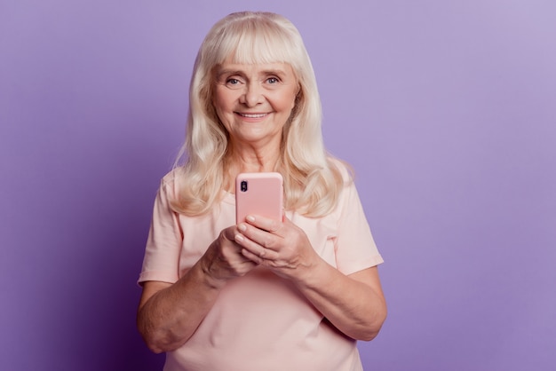 Foto de uma velha usando smartphone isolada sobre fundo violeta