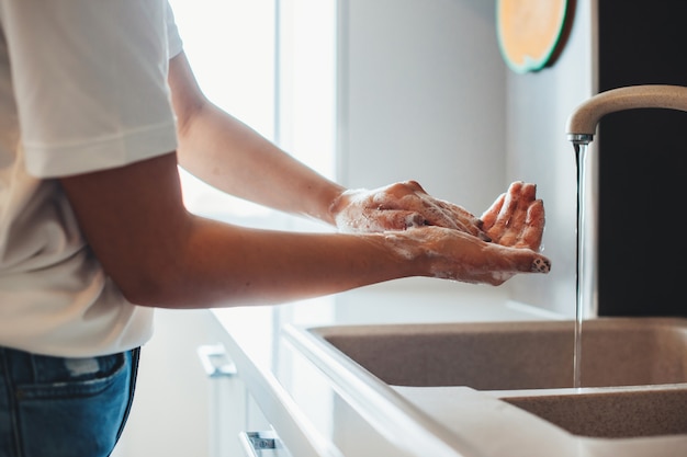 Foto de vista lateral de um homem lavando as mãos na cozinha com sabonete