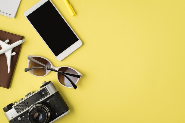 Foto de vista superior da câmera de óculos de sol de caneta de notebook de exibição de smartphone e modelo de avião na capa do passaporte em fundo amarelo pastel isolado com copyspace