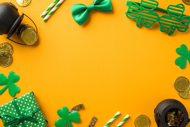 Foto de vista superior da decoração do dia de são patrício óculos de festa em forma de trevo canudos gravata borboleta verde caixa de presente trevos ferradura potes com moedas de ouro em fundo amarelo isolado com espaço em branco no meio