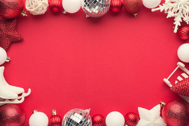 Foto de vista superior de bolas de discoteca decorações de árvore de natal branco e vermelho estrelas floco de neve pequeno trenó e patins de gelo em fundo vermelho isolado com espaço vazio no meio