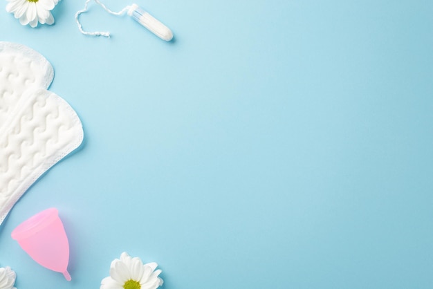 Foto de vista superior de botões de flores de camomila absorventes higiênicos copo menstrual rosa e tampão em fundo azul pastel isolado com copyspace