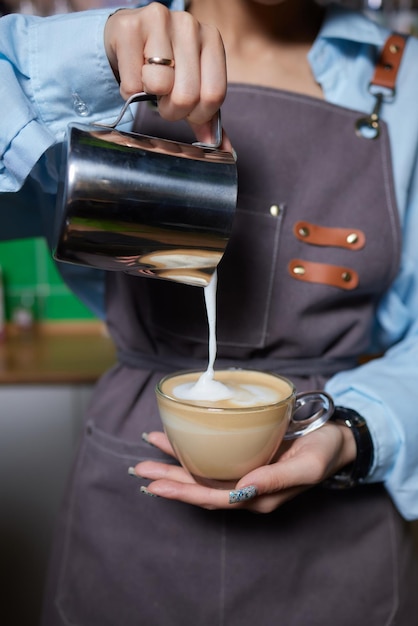 Foto de vista superior do barista profissional derramando leite do pote para uma xícara de café sendo prepa