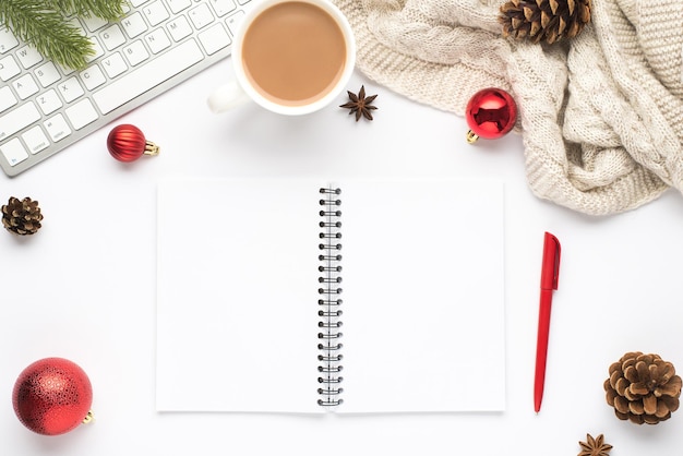 Foto de vista superior do copo de teclado de caneta de planejador aberto de bebida quente vermelho bolas de árvore de natal cones de galho de pinho anis e cachecol aconchegante em fundo branco isolado com espaço vazio