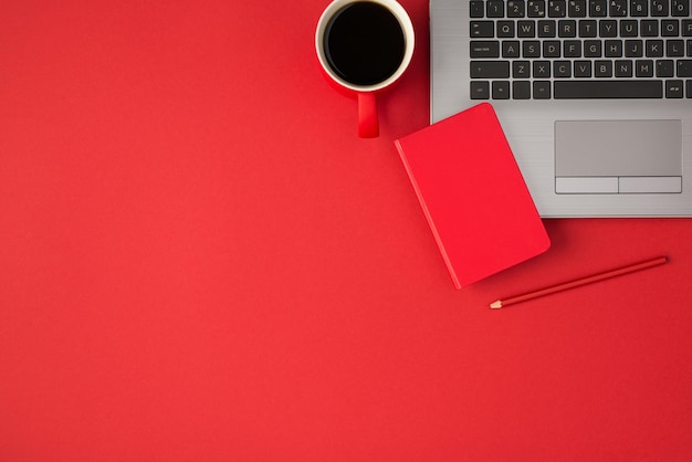 Foto de vista superior do pequeno caderno vermelho fechado no laptop lápis vermelho e xícara de bebida em fundo vermelho isolado com espaço vazio