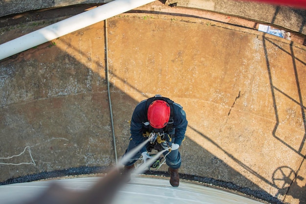 Foto de vista superior do soldador de acesso por corda industrial trabalhando em altura usando equipamento de segurança de capacete de arnês inspeção de acesso por corda do tanque de armazenamento de espessura